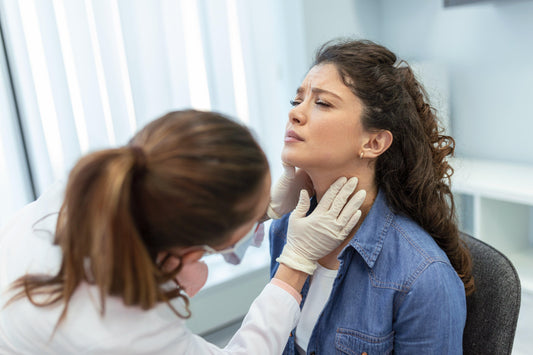 woman in doctor's office.  doctor is examining sore throat of patient.